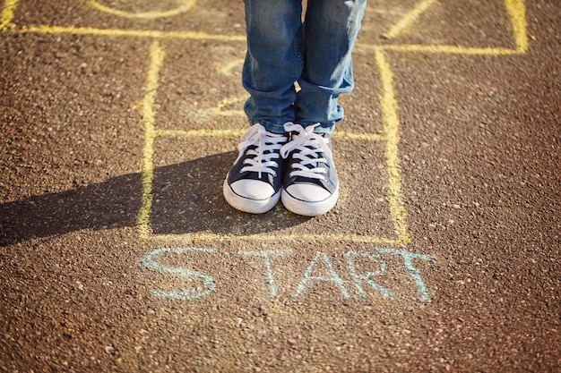 Primo piano delle gambe del ragazzo e giocare a campana sul parco giochi all&#39;aperto. Hopscotch gioco di strada popolare