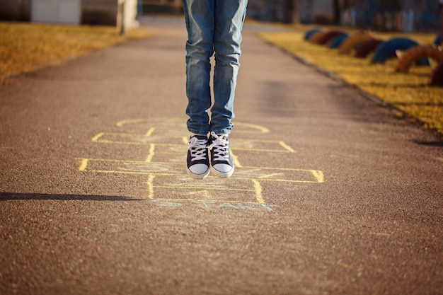 Primo piano delle gambe del ragazzo e giocare a campana sul parco giochi all&#39;aperto. Hopscotch gioco di strada popolare