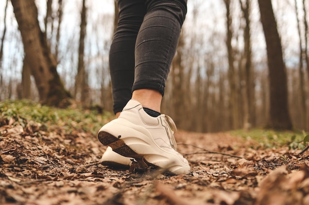 Primo piano delle gambe di una donna che corre nella foresta Scarpe sportive Alberi e foglie sullo sfondo Concetto di stile di vita attivo e sano