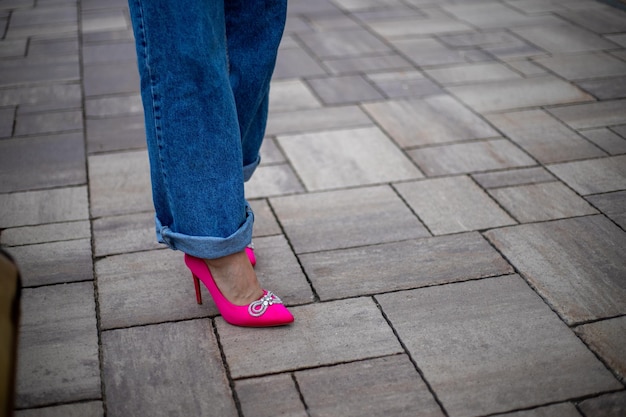 primo piano delle gambe di una donna in jeans con scarpe con tacco alto fucsia brillante sulla strada