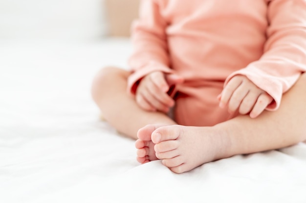 Primo piano delle gambe e delle braccia di un bambino piccolo su un letto bianco chiaro