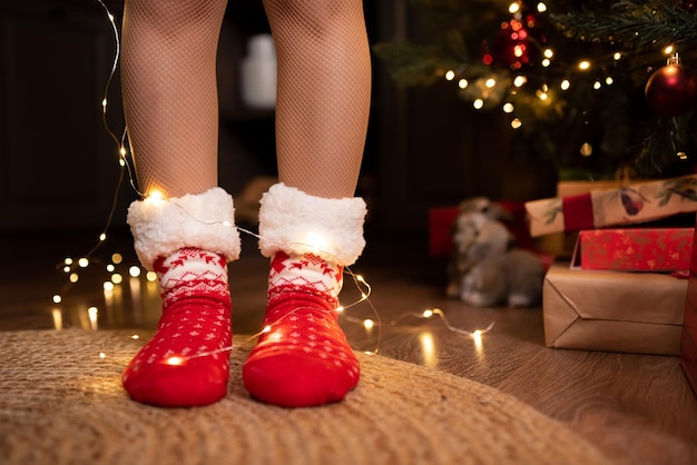 Primo piano delle gambe femminili in calzini rossi di Natale Accanto a lei si trova un cappello rosso di Babbo Natale Celebrazione del Natale del nuovo anno