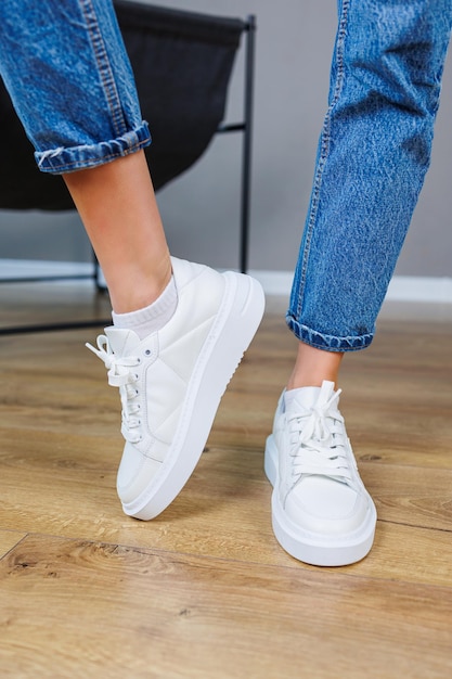 Primo piano delle gambe femminili in jeans e sneakers bianche casual Scarpe casual comode da donna Sneakers da donna in pelle bianca