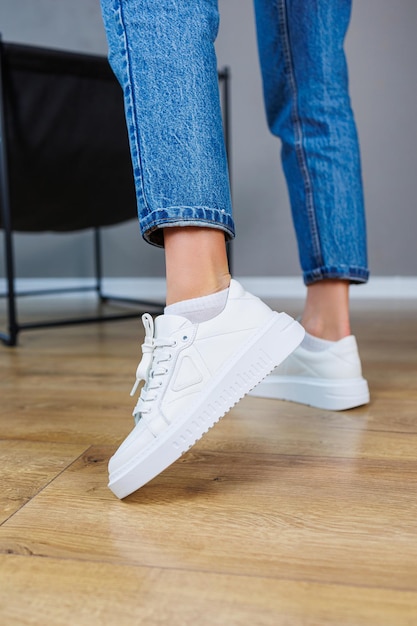 Primo piano delle gambe femminili in jeans e sneakers bianche casual Scarpe casual comode da donna Sneakers da donna in pelle bianca