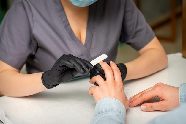 Primo piano delle mani caucasiche di un manicure professionista stanno limando le unghie di una giovane donna Giovane donna caucasica che riceve una manicure da un'estetista con una lima per unghie in un salone di bellezza