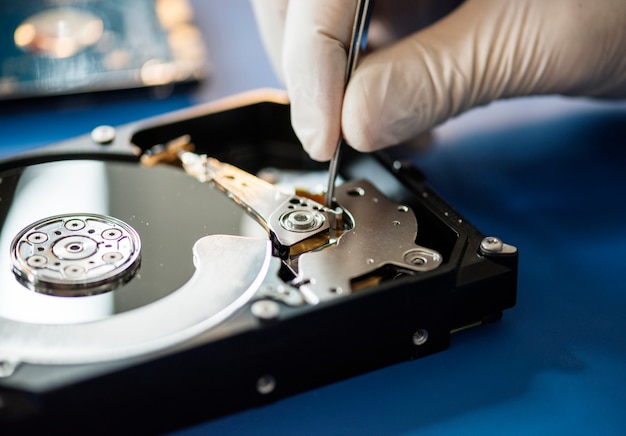 Primo piano delle mani con pinzette e disco rigido del computer