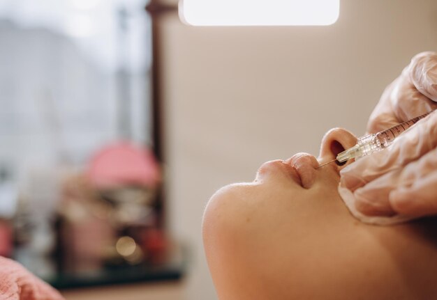 Primo piano delle mani del cosmetologo che fa l'iniezione di botox nelle labbra femminili Sta tenendo la siringa La giovane bella donna sta ricevendo la procedura con divertimento