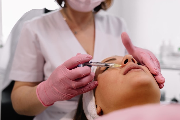 Primo piano delle mani del cosmetologo che fa l'iniezione di botox nelle labbra femminili Sta tenendo la siringa La giovane bella donna sta ricevendo la procedura con divertimento