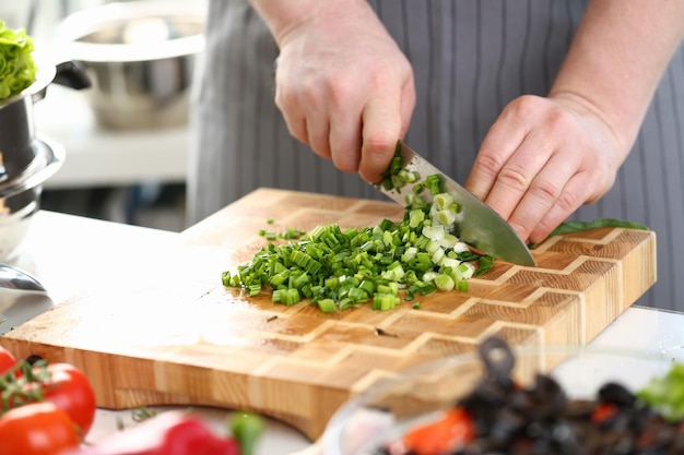 Primo piano delle mani del cuoco che tiene il coltello per tagliare le cipolle verdi