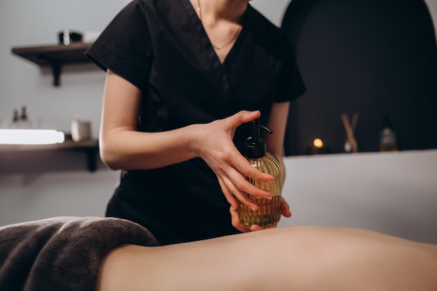 Primo piano delle mani del massaggiatore che versano olio aromatico sulla schiena della donna La massaggiatrice si prepara a fare la procedura spa orientale per un trattamento rilassante Terapista che fa massaggio con olio aromaterapico sul corpo della donna