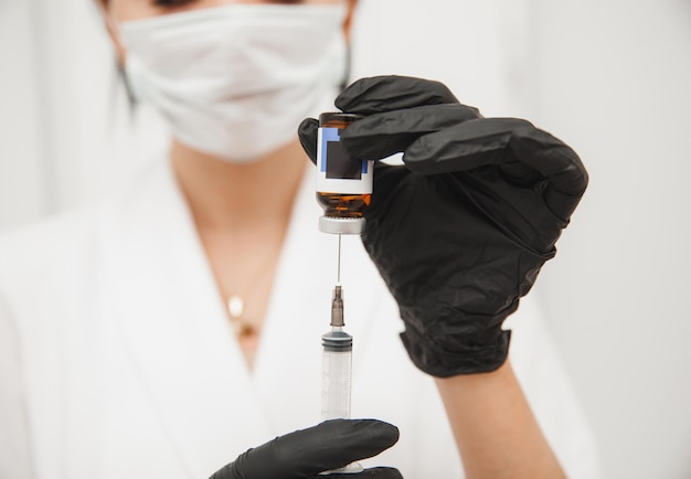 Primo piano delle mani del medico in guanti protettivi sterili che prelevano una siringa da una fiala con un vaccino Spazio di sfondo bianco per il testo
