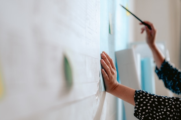 Primo piano delle mani dell'architetto femminile che scrivono il modello a bordo Sfocato dietro il team di ingegneri