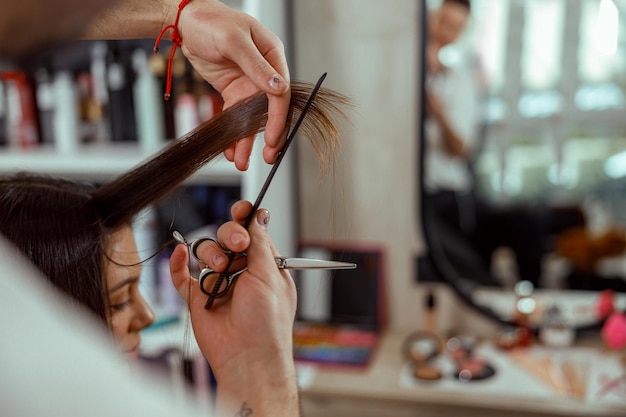 Primo piano delle mani dell'estetista con un pettine che taglia i capelli della donna