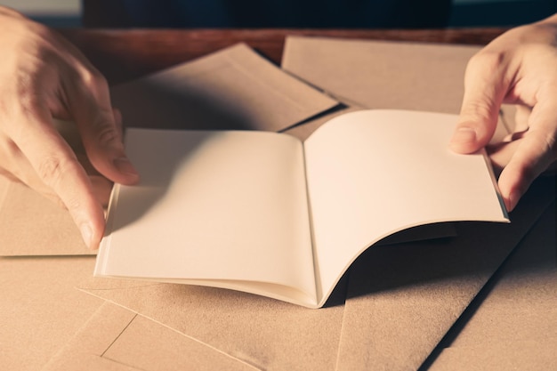 Primo piano delle mani dell'uomo bello che aprono il libro bianco in bianco sui precedenti di legno marrone del tabel