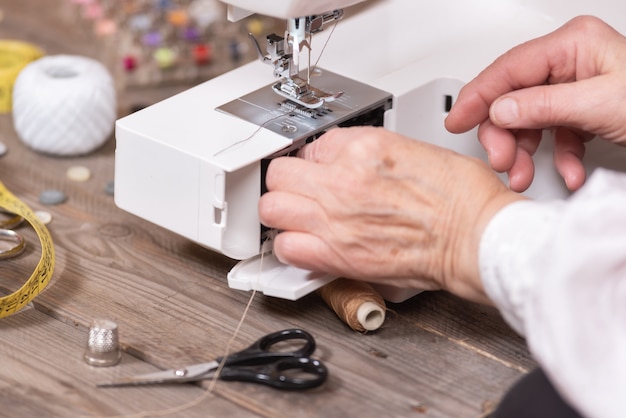 Primo piano delle mani della cucitrice senior della donna che rimuovono la custodia della bobina