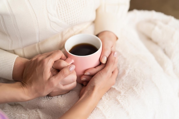 Primo piano delle mani della donna anziana che tengono una tazza rosa del concetto di Hugge o Lagom di tè aromatico