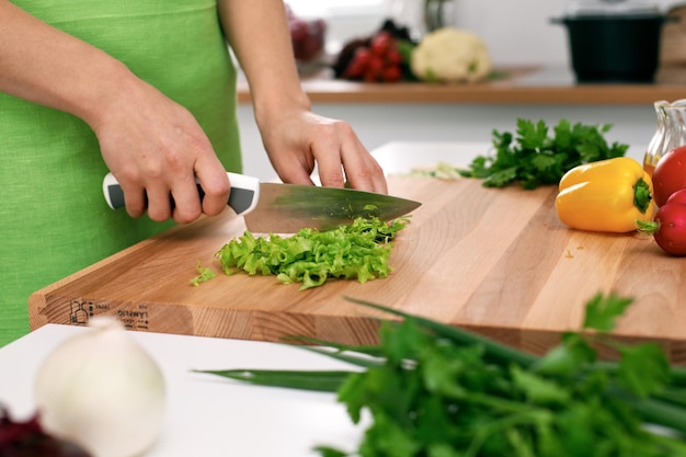 Primo piano delle mani della donna che cucinano in cucina Casalinga che affetta insalata fresca