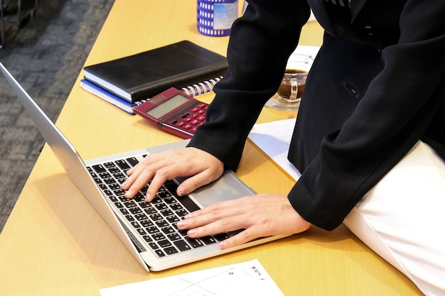 Primo piano delle mani della donna che digitano sulla tastiera del computer portatile nel suo posto di lavoro presso l&#39;ufficio