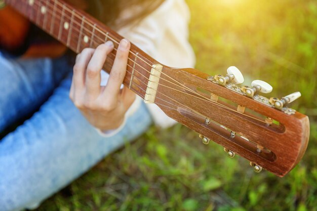 Primo piano delle mani della donna che suonano la chitarra acustica sullo sfondo del parco o del giardino. Ragazza teenager che impara a suonare una canzone e a scrivere musica. Hobby, stile di vita, relax, strumento, tempo libero, concetto di educazione