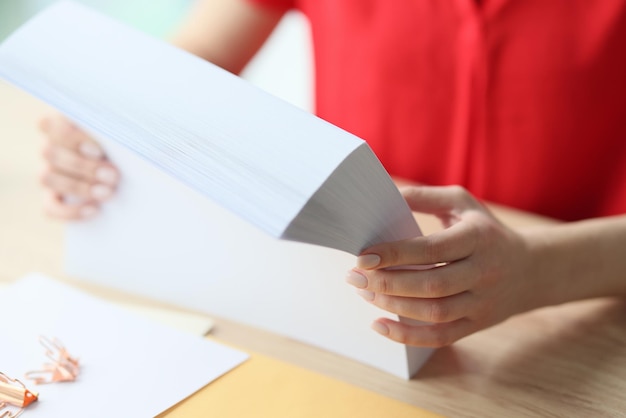 Primo piano delle mani della donna che tengono pila di fogli bianchi di carta sul posto di lavoro degli impiegati dell'ufficio