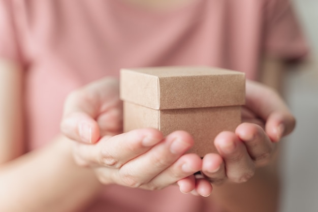 Primo piano delle mani della donna che tengono una piccola confezione regalo. Piccola scatola regalo nelle mani della donna.