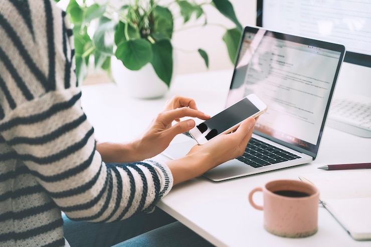 Foto primo piano delle mani della donna con smartphone e laptop alla scrivania