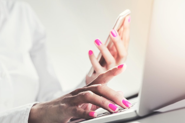 Primo piano delle mani della donna d'affari con smalto rosa che tiene uno smartphone e digita con la lancetta dei secondi. Immagine tonica