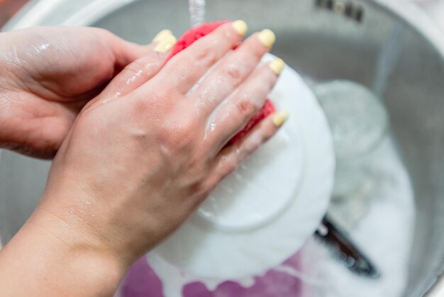 Primo piano delle mani della donna di lavare i piatti nel lavello della cucina Lavori di pulizia