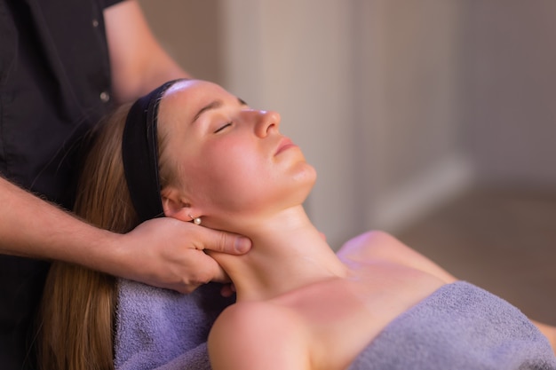 Primo piano delle mani della massaggiatrice che massaggiano il viso femminile donna occhi chiusi con piacere