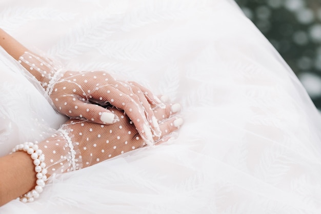 Primo piano delle mani della sposa in guanti bianchi trasparenti vicino a una cascata nel parco. Un modello in abito da sposa e guanti in rete in un parco naturale. Bielorussia