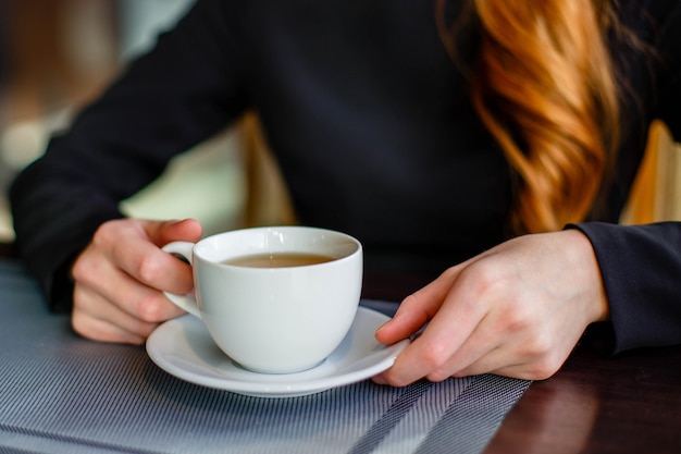 Primo piano delle mani delle donne con la tazza del tè verde mentre sedendosi in caffè comodo
