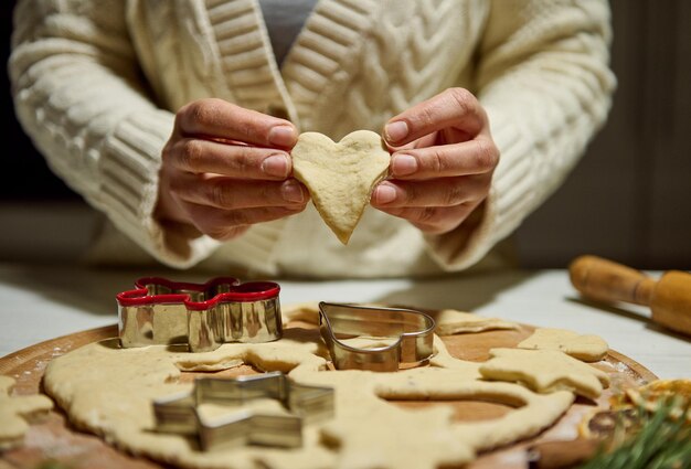 Primo piano delle mani dello chef che tengono l'impasto di pan di zenzero tagliato a forma di cuore mentre preparano i biscotti di Natale