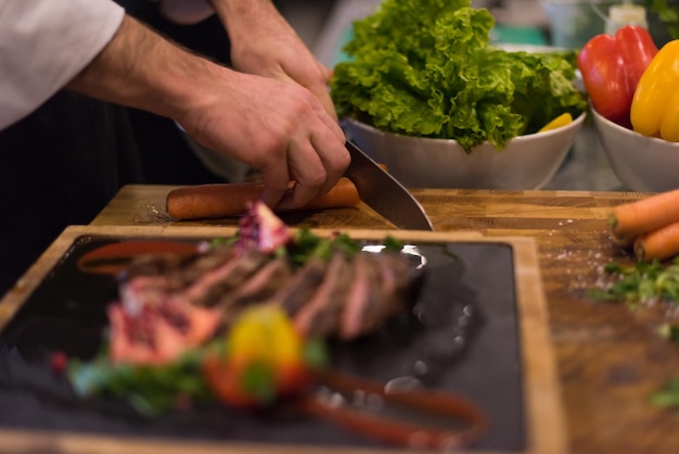 primo piano delle mani dello chef nella cucina dell'hotel o del ristorante che preparano bistecca di manzo con decorazione vegetale