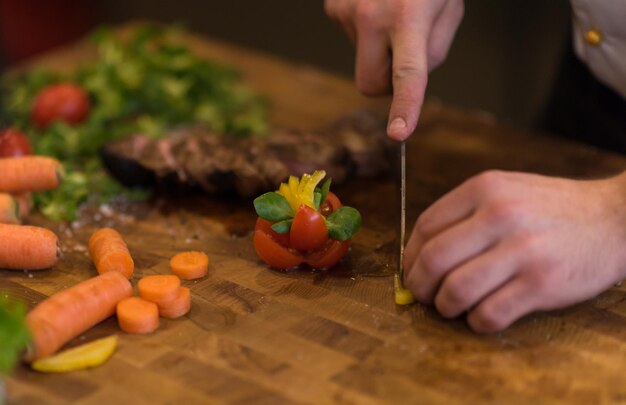 primo piano delle mani dello chef nella cucina dell'hotel o del ristorante che preparano bistecca di manzo con decorazione vegetale