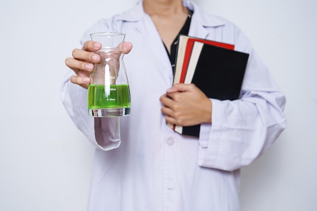 Primo piano delle mani dello scienziato in un camice bianco che tiene vetreria chimica e libri.