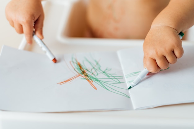 Primo piano delle mani di un bambino piccolo disegno con pennarelli colorati sulla carta. Attività creativa