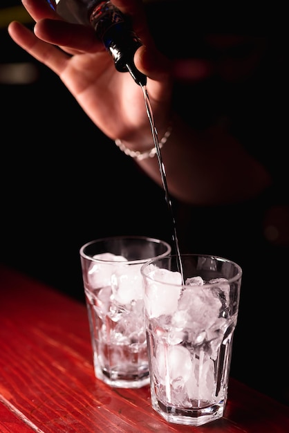 Primo piano delle mani di un barista che versa una bevanda alcolica per fare un cocktail in un bicchiere di vetro