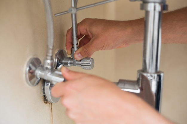 Primo piano delle mani di un idraulico e scarico del lavabo