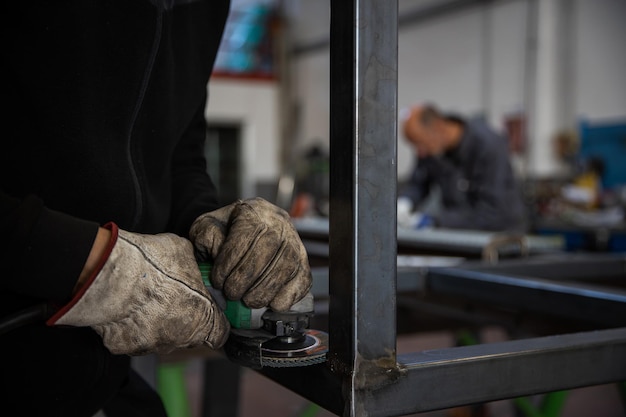 Primo piano delle mani di un lavoratore che utilizza la levigatrice su una barra di metallo indossando guanti protettivi