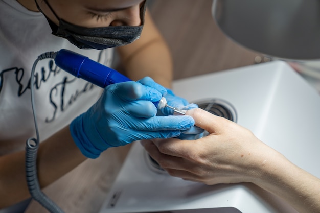 Primo piano delle mani di un maestro di manicure in cui uno strumento speciale per rimuovere la vernice