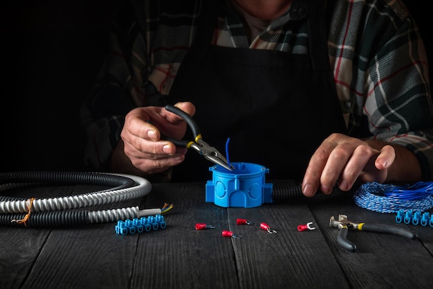 Primo piano delle mani di un maestro elettricista durante il lavoro Installazione di cavo o filo alla scatola di giunzione blu