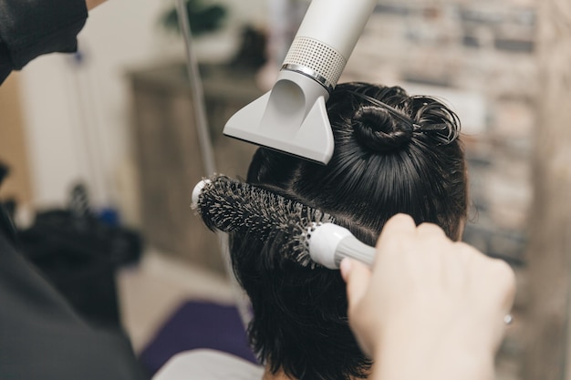 Primo piano delle mani di un parrucchiere che asciuga i capelli delle donne con un asciugacapelli taglio di capelli corto e styling