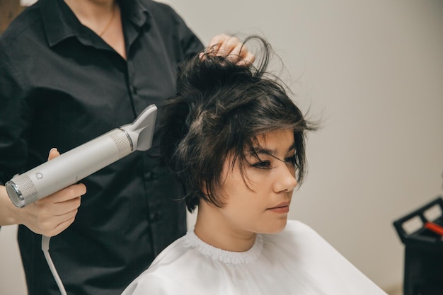 Primo piano delle mani di un parrucchiere che asciuga i capelli delle donne con un asciugacapelli taglio di capelli corto e styling