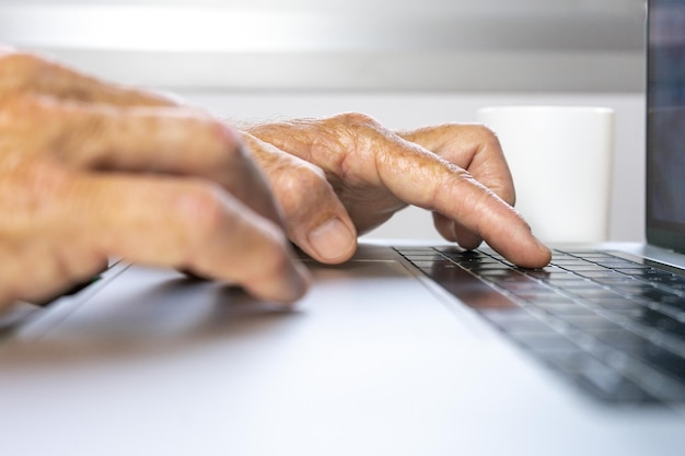Primo piano delle mani di un uomo più anziano che lavora su un computer portatile