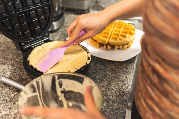 Primo piano delle mani di una donna che mette la pasta in una piastra per cialde