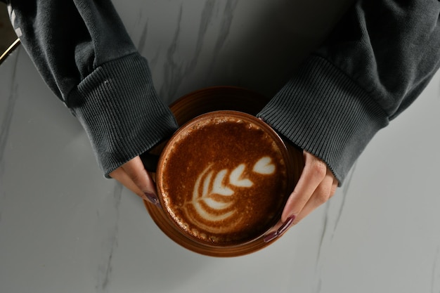 Primo piano delle mani di una donna che tiene una tazza di caffè americano con schiuma spessa, cappuccino caldo,