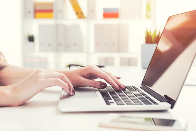 Primo piano delle mani di una donna elegante con una buona manicure che digita sulla tastiera di un laptop in un ufficio bianco. Concetto di una routine d'ufficio. Immagine tonica