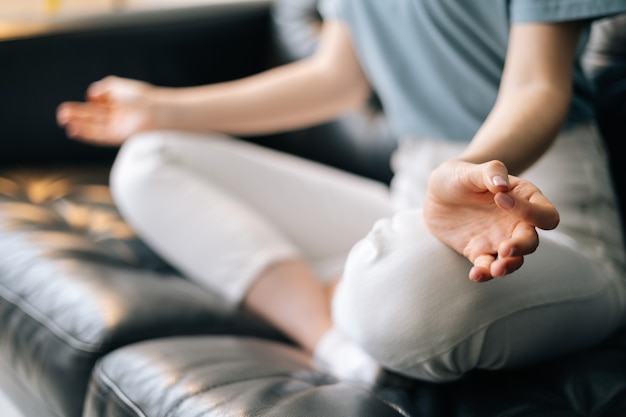 Primo piano delle mani di una donna irriconoscibile che si tiene per mano nel mudra che pratica yoga a casa