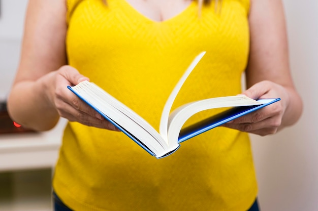 Primo piano delle mani di una donna vestita di giallo che apre un libro