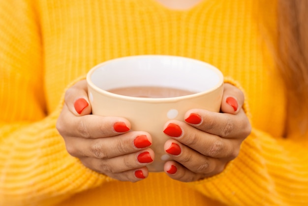 Primo piano delle mani di una ragazza con una tazza di tè caldo e gustoso